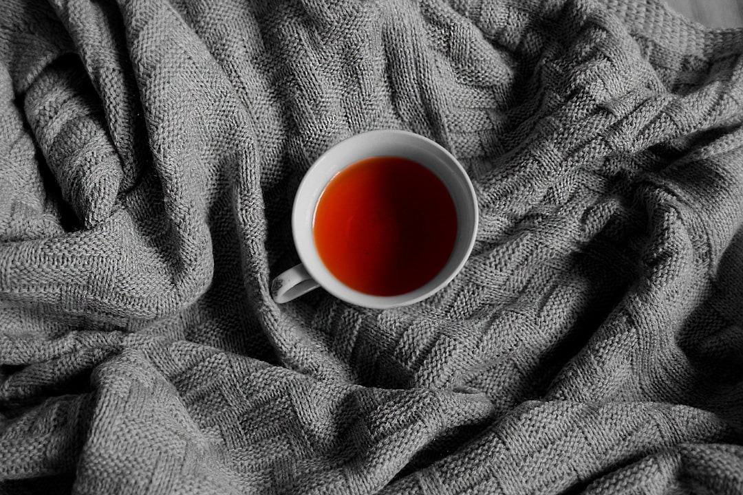 A white teacup filled with tea sits on a knitted blanket.